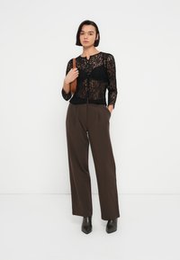 Μαύρο τοπ από δαντέλα με μανίκια τριών τετάρτων, κλείσιμο με κουμπιά και στρογγυλή λαιμόκοψη, συνδυασμένο με καφέ παντελόνια ψηλόμεσα και μαύρα μποτάκια αστραγάλου.