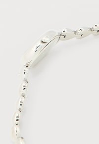 Εγγύς πλάνο ενός γυαλισμένου ασημένιου βραχιολιού με οβάλ συνδέσμους και ορθογώνιο κούμπωμα με ένα μικρό κουμπί.