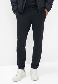 Pantaloni jogger navy in tessuto leggero e elastico, con tasche laterali e vita elasticizzata; abbinati a sneaker bianche con suole testurizzate.