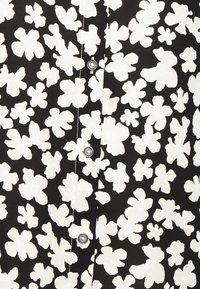 Camicia nera in tessuto con grande motivo floreale bianco, dotata di bottoni argentati e design con chiusura a bottoni.