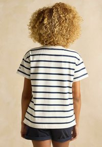 Valge ja tumesinine triibuline lühikeste varrukatega särk, millel on ümmargune kaelus ja külgmised lõhikud, koos tumedate lühikeste pükstega.