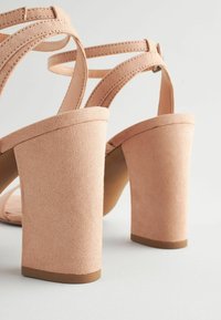 Blush rosa högklackade sandaler med mocka-textur, tjocka blockklackar och flera korsade remmar för stöd.