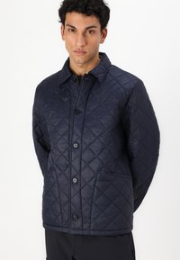 Jachetă cu quilt de culoare bleumarin, cu guler, nasturi în față, două buzunare laterale și un model de diamante cusut. Ușoară, cu o textură netedă.