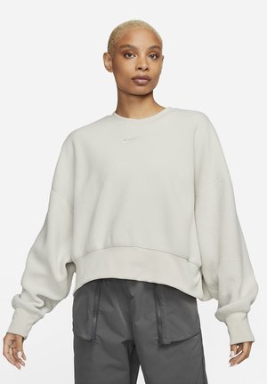 Sweatshirt en polaire gris clair avec un col rond et des épaules tombantes. Présente un logo Nike discret sur la poitrine et un ourlet côtelé.