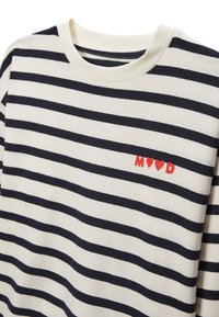 Chemise à manches longues rayée en crème et bleu marine, avec un col rond et des lettres rouges accompagnées d'un motif de cœur sur la poitrine.