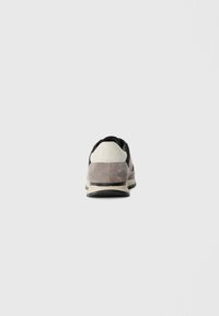 Pantofii sport cu partea superioară din suede gri și negru, având un tab de călcâi alb, talpă amortizată și accente din plasă texturată.