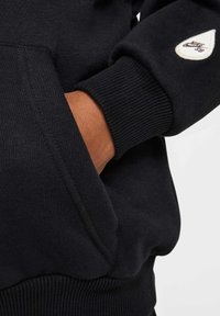 Sweatshirt de un albastru închis, cu manșete și tiv cu nervuri. Dispune de un buzunar lateral și un mic etichetă Nike SB pe mânecă. Textură moale.