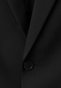 Czarna marynarka z wyraźnie zaznaczonym kołnierzem, gładką fakturą materiału oraz okrągłym czarnym guzikiem z subtelnym kwiatowym wzorem.