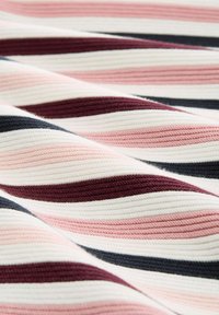 Megztas audinys su banguotomis juostomis rožinės, baltos, tamsiai raudonos ir tamsiai mėlynos spalvos. Paviršius atrodo raukšlėtas, sukuriant sluoksniuotą vizualinį efektą.