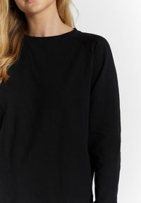 Maglietta nera a maniche lunghe realizzata in un tessuto morbido e liscio con scollatura rotonda e maniche raglan, caratterizzata da un design semplice ed elegante.
