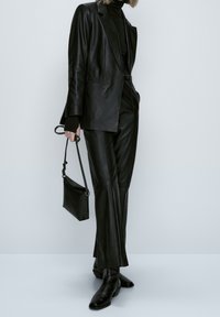 Zwarte leren blazer en broek met een aansluitende zwarte turtleneck, gecombineerd met een kleine zwarte handtas en puntige zwarte enkellaarzen.