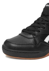 Czarny sportowy but z teksturowaną skórzaną cholewką, płaskimi czarnymi sznurówkami, białym logo, gumową podeszwą i zaokrąglonym noskiem.