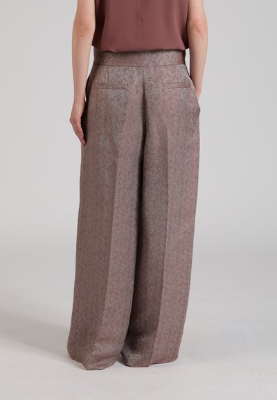 Persona che indossa pantaloni marroni a vita alta, a gamba larga e con trama, e una canotta marrone senza maniche, vista da dietro su sfondo semplice.