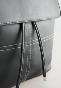 Sac en cuir gris avec une fermeture à rabat, coutures blanches, détail de cordon de serrage et texture lisse.