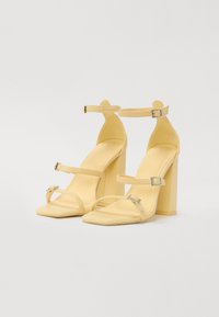 Yellow high-heeled sandals with a square toe and block heel. Features two ankle straps with adjustable buckles and a smooth finish.
