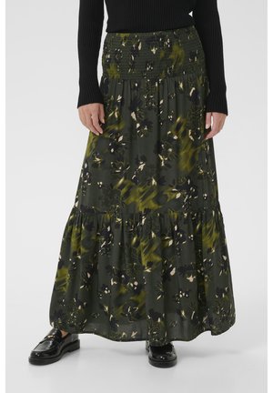 Jupe midi fleurie en vert foncé, avec une taille smockée, un design en plusieurs niveaux, ornée de motifs abstraits en crème et noir. Portée avec des chaussures noires.