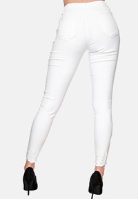Jeans blancos ajustados con cintura alta, cinco bolsillos, detalles deshilachados en los tobillos y una textura suave, combinados con zapatos de tacón altos negros.