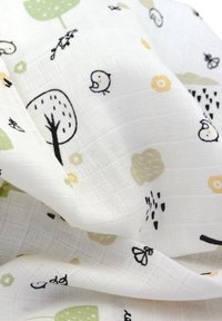 Witte stof met lichtgroene bomen, gele bloemen en zwarte vogels, kenmerkend door een gestructureerd, geweven oppervlak en verspreide speelse patronen.