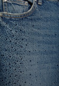 Modré džínsy z denimu s vode odpudivou úpravou, na povrchu sú kvapky vody rôznych veľkostí, detailné prešívanie a kovové doplnky.