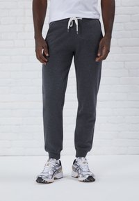 Ciemnoszare dresy wykonane z miękkiego, teksturowanego materiału, z elastycznym mankietem w pasie i białymi sznurkami regulacyjnymi, z tapered nogawkami i bocznymi kieszeniami.