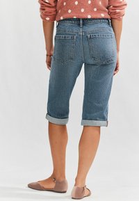 Jeans Bermuda-shorts i mellanblått, med uppvikta ärmar och bakfickor, bärs med taupe ballerina, minimalistisk design utan dekorationer.