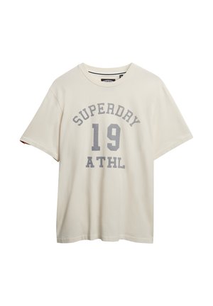 T-shirt couleur crème en coton, avec un col rond et des manches courtes. Il présente un texte imprimé gris : "SUPERDAY 19 ATHL."