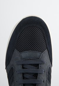 Sneaker blu navy con tomaia in pelle e mesh testurizzati, punta rotonda e lacci piatti. La suola è bianca con un motivo di presa testurizzato.
