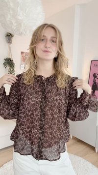 Braune, transparente Bluse mit floralem Muster in Hellrosa, mit einer Krawatten-Halsöffnung und Knopfverschluss, langen Ärmeln und leicht rüschigem Saum.