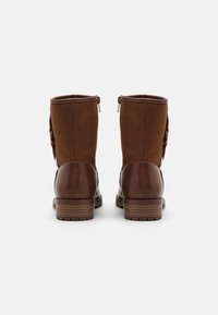 Bottes en cuir marron à la cheville, alliant suède et cuir, avec une fermeture éclair et une semelle texturée marron.