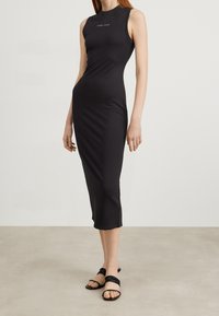 Svart ärmlös klänning i stretchigt material, med en figursydd silhuett och längd till mitten av vaden. Logotypen "TOMMY JEANS" tryckt framtill.