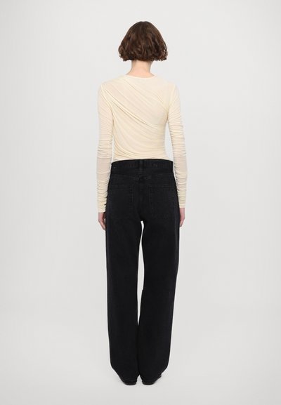 Long-sleeve light beige top with twisted texture, paired with high-waisted black wide-leg jeans featuring back pockets and a relaxed fit.
