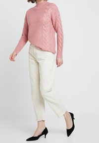 Ljusrosa kabelstickad tröja med hög halsringning, kombinerad med off-white korta jeans och svarta spetsiga klackskor.