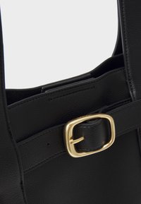 Borsa a tracolla nera in pelle con finitura testurizzata, dotata di una fibbia in metallo dorato e di un manico piatto. Include un'apertura superiore per l'accesso.