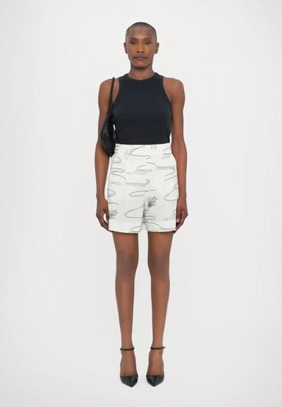 Μαύρη αμάνικη μπλούζα, λευκές σορτς με σχέδια σε αφηρημένες γραμμές, ψηλόμεση σχεδίαση, συνδυασμένα με μαύρες μυτερές γόβες και μια μικρή τσάντα.