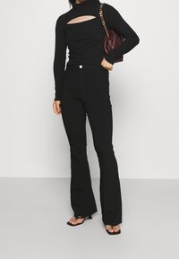Black long-sleeve top with a cutout detail, fitted silhouette, paired with high-waisted black flared pants and black strappy sandals.