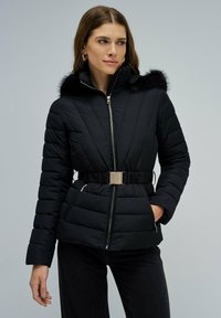 Chaqueta acolchada negra con capucha de piel sintética, diseño acolchonado diagonal, cierre de cremallera, cintura ajustada con hebilla metálica y dos bolsillos con cremallera.