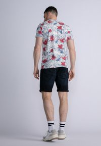 Camiseta con estampado floral con flores rojas y azules sobre un fondo blanco, combinada con pantalones cortos oscuros. El calzado presenta un esquema de colores en gris y blanco.