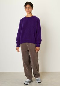 Maglione di lana viola con spalle scese, polsini e orlo a coste. Abbinato a pantaloni in corduroy marrone chiaro e scarpe sportive grigie.