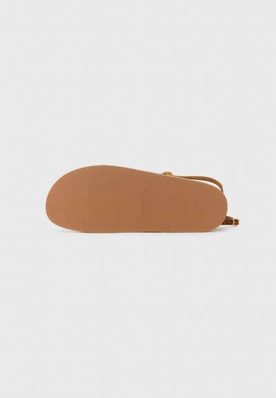 Brun gummisula på en sko med ett strukturerat greppmönster, som har ett justerbart rem och en platt design.