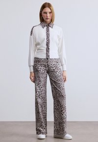 Λευκό φούτερ με γιακά και λεπτομέρειες με λεοπάρ εκτύπωση, συνδυασμένο με φαρδιά παντελόνια που διαθέτουν αντίστοιχο σχέδιο λεοπάρ. Λευκά παπούτσια.