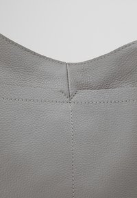 Harmaa nahkalaukku, jossa on sileä pinta, ja näkyvät saumat sekä kaareva yläreunamuotoilu. Yksinkertainen ja minimalistinen ilme.