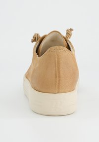 Baskets en daim beige avec un talon arrondi, semelle en caoutchouc blanc et accents décoratifs torsadés à l'arrière pour un détail supplémentaire.