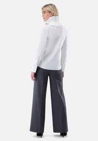 White blouse with a ruffled collar, paired with dark gray wide-leg trousers. Smooth fabric texture and tailored design. Black heels.