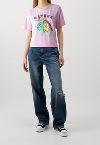 Pink cropped t-shirt with graphic print featuring a parrot and leaves, paired with baggy blue jeans with a distressed knee, and black sneakers.