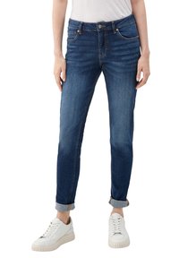 Vaqueros de mezclilla en lavado oscuro, corte ajustado, con cintura de altura media, cuatro bolsillos y puños remangados. Combinados con zapatillas blancas.