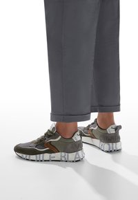 Sneaker olivastro e grigio in materiale mesh e suede, con suola in gomma, branding distintivo e design della punta arrotondata.