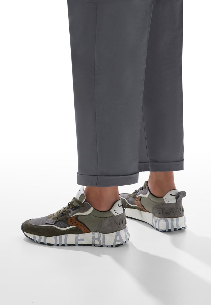 Sneaker olivastro e grigio in materiale mesh e suede, con suola in gomma, branding distintivo e design della punta arrotondata.