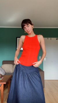 Camisola de alças vermelha com uma silhueta ajustada, combinada com uma saia maxi de denim escuro e fluida, com cintura pregueada. Acessórios incluídos: brincos de argola dourados.