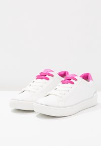 Bílé tenisky s růžovými tkaničkami a vnitřním podšíváním, hladký materiál, zaoblená špička, kovový akcent na patě a jednoduchý design.