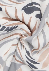 Tessuto decorato in tonalità di grigio, blu navy e beige. Presenta disegni di foglie avvolgenti su uno sfondo bianco con una superficie liscia.